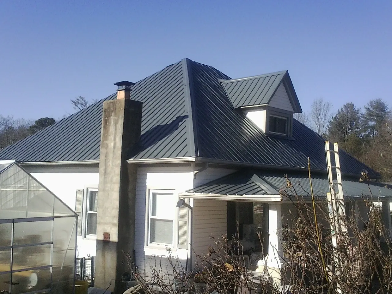 Dark blue standing seam metal roof on a white farmhouse with dormer — Slate & Tile Roof Repair by Roofing Brothers in Connell