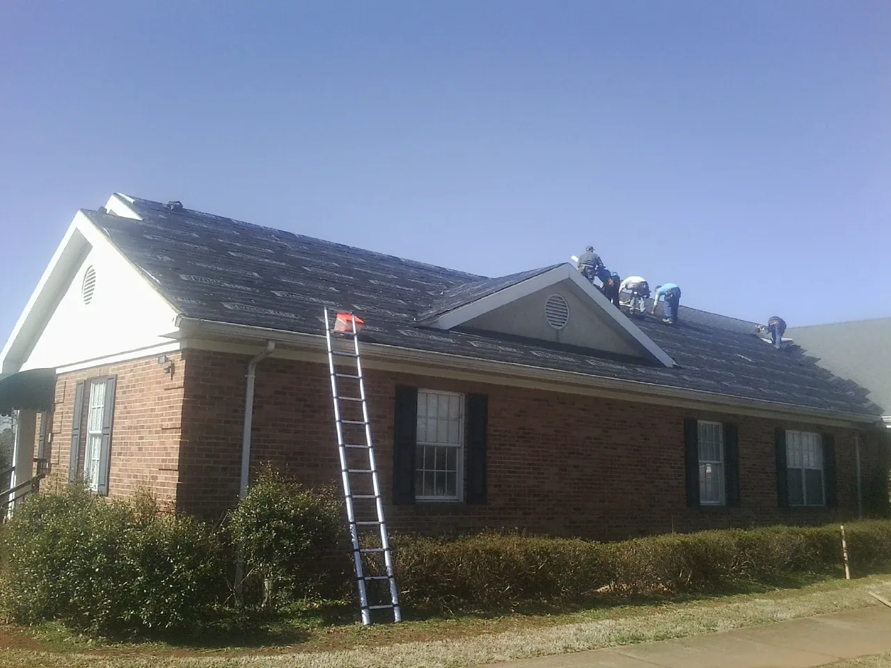 Crew tearing shingles off a brick ranch roof with a ladder set — Emergency Roof Repair work by our crew in Connell